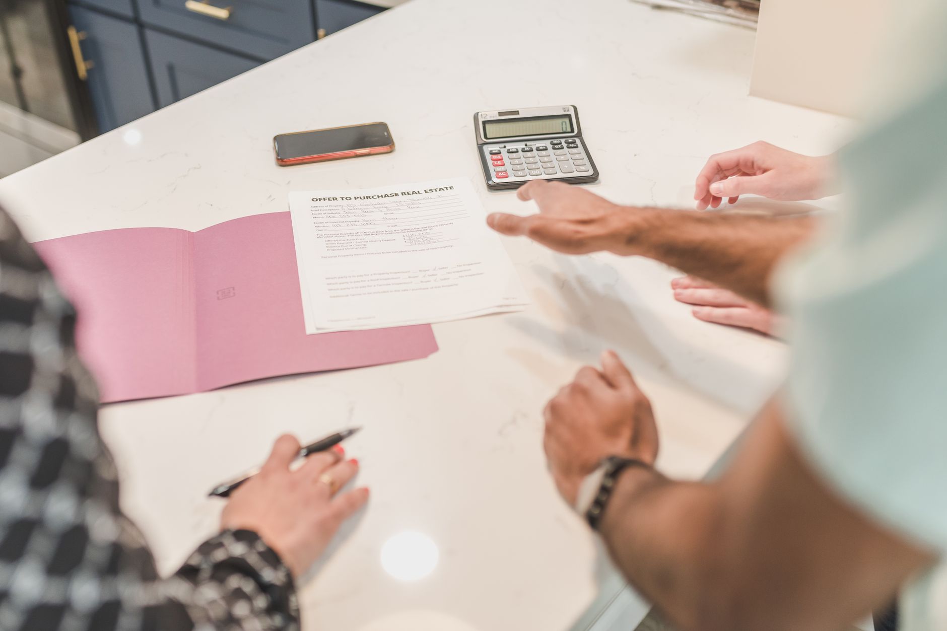 Manos sobre una mesa de cocina de mármol con un documento inmobiliario, una calculadora y un teléfono móvil.